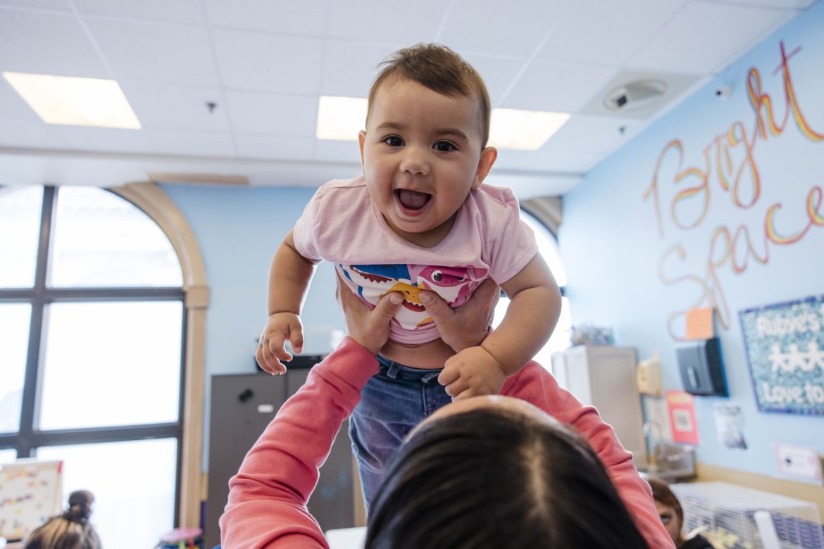 An adult holds a smiling baby in the air.